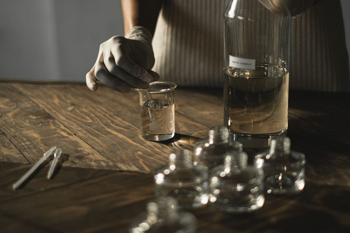 Fragrance development: a gloved hand measuring fragrance into a beaker beside glass bottles